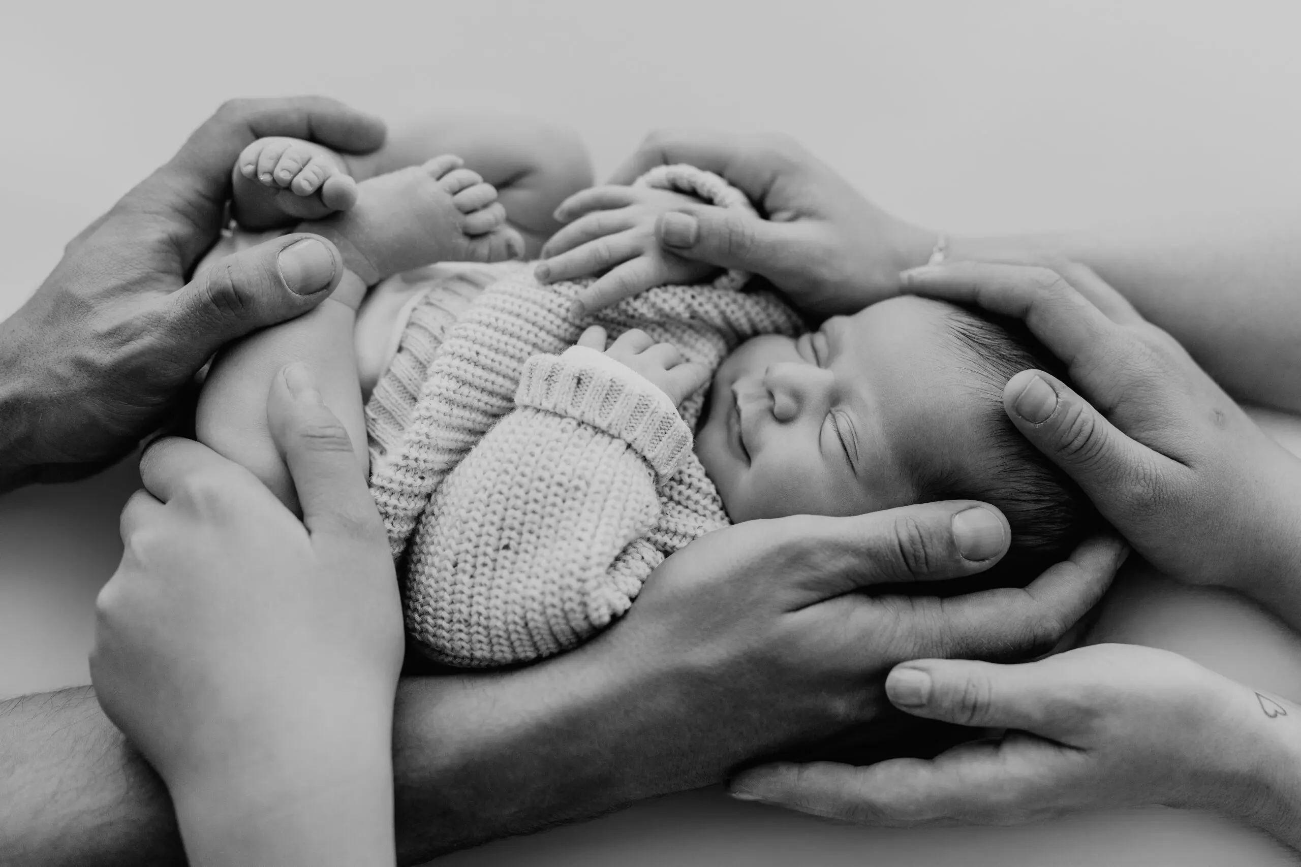 Schlafendes Neugeborenes in gestricktem Outfit wird in Händen gehalten – Neugeborenenfotografie