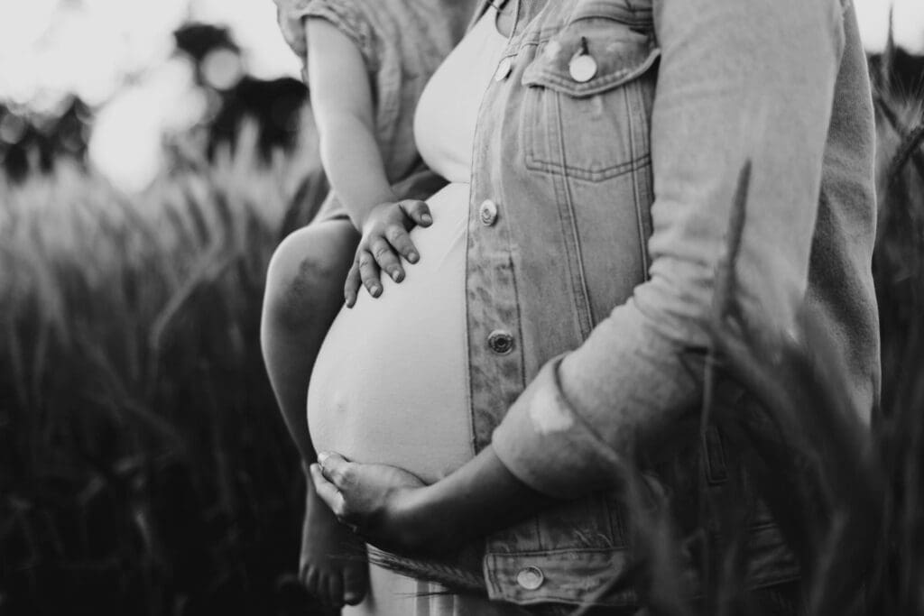 Babybauchaufnahme in Schwarzweiß, Geschwisterkind und Mama streicheln gemeinsam den Bauch