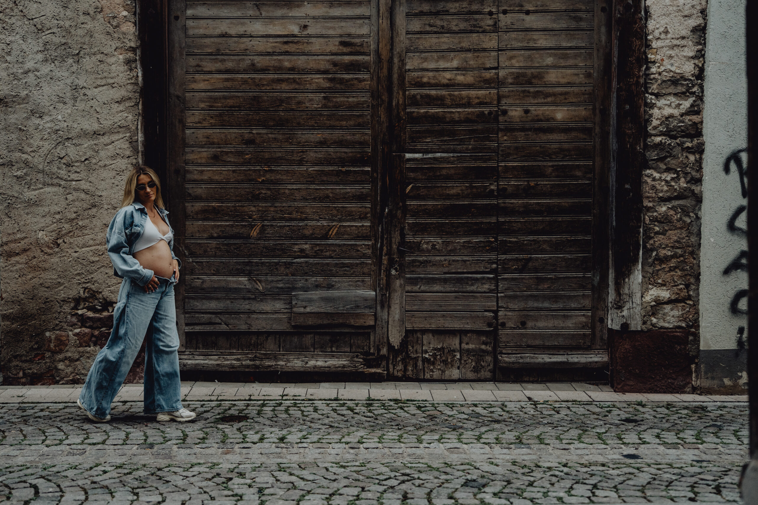 urbane Babybauchaufnahme, Frau in Jeanslook, Babybauch frei, läuft an einem Tor