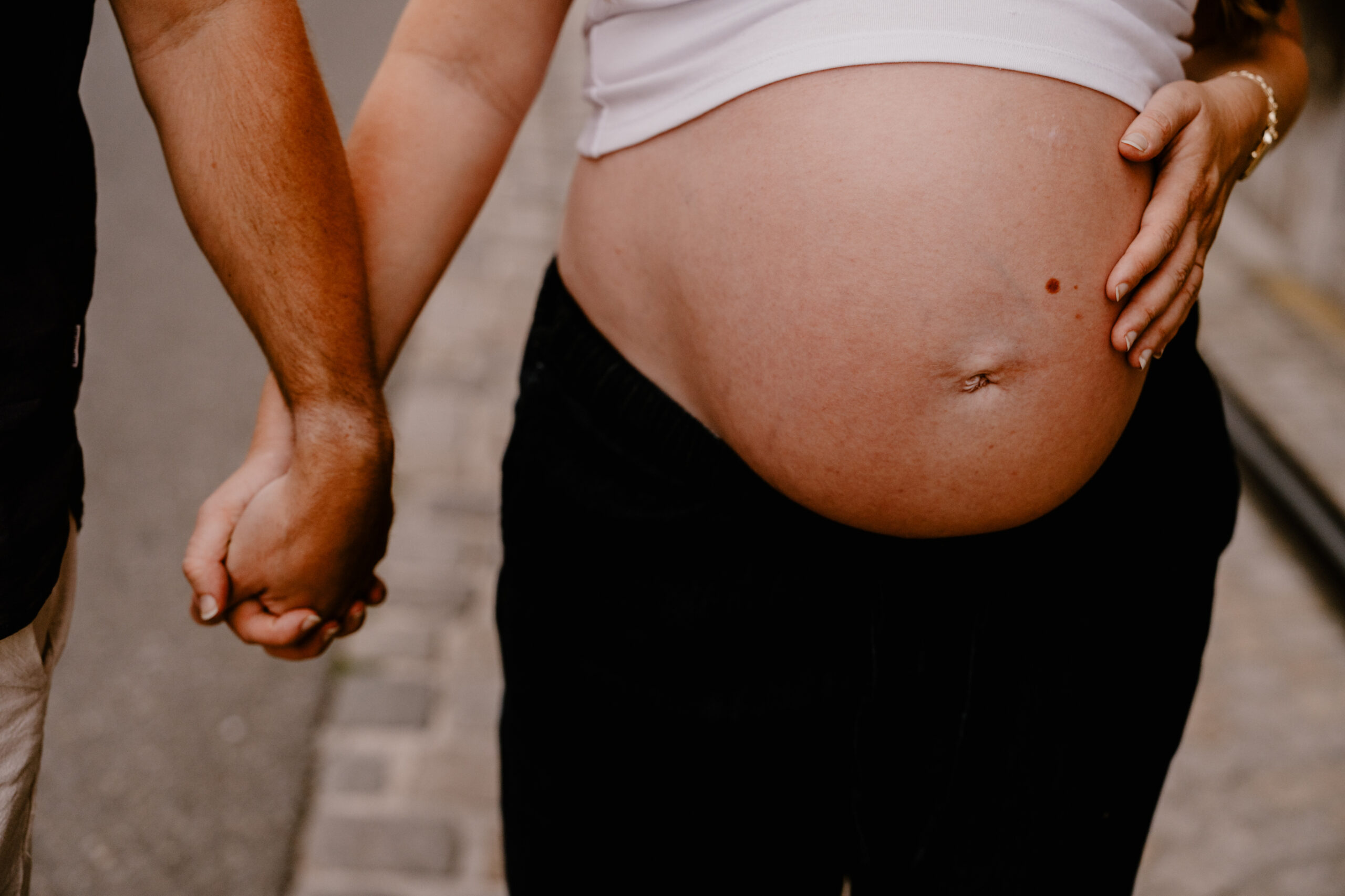 Babybauchshooting in der City, Babybauch im Fokus, Pärchen läuft Hand in Hand