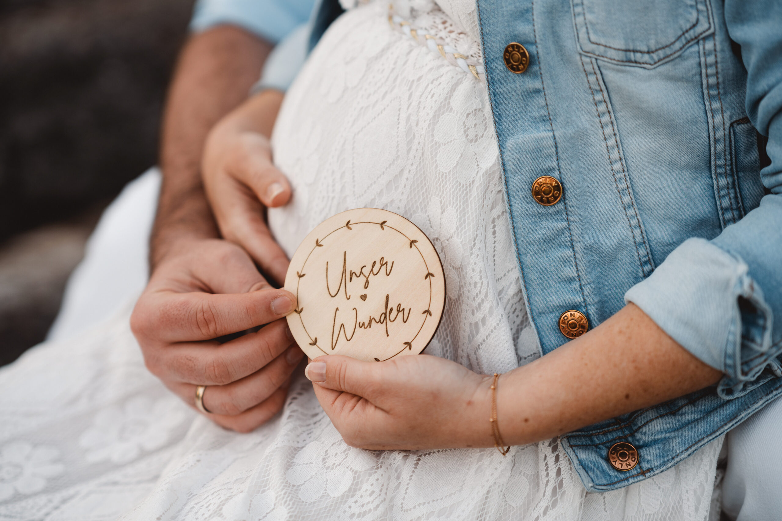 Bbybauchaufnahme mit Fokus auf Babybauch, kleine Holzscheibe in der Hand vor dem Bauch